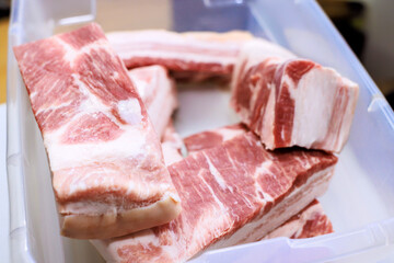 Fototapeta premium Several pieces of raw pork belly are arranged in clear plastic container on kitchen counter for cooking.