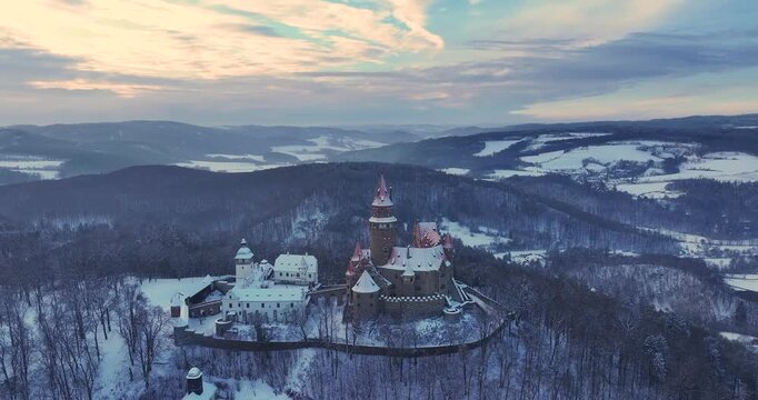 Aerial drone footage of Bouzov Castle covered in snow at sunrise in the Czech Republic. Cinematic winter landscape with medieval architecture, ideal for: travel films, history, tourism promotion.
