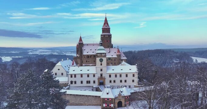 Aerial drone footage of Bouzov Castle covered in snow at sunrise in the Czech Republic. Cinematic winter landscape with medieval architecture, ideal for: travel films, history, tourism promotion.