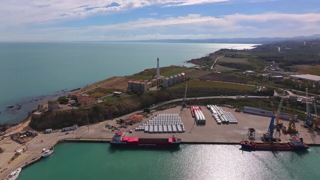 Aerial view of Vasto port with cargo ships, small boats, calm sea, blue sky and surrounding coastline.
