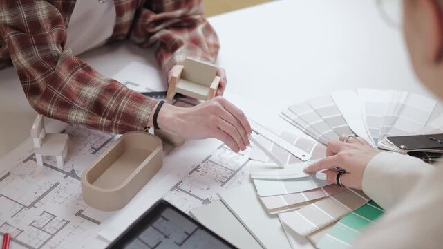 Interior design planning with architectural models and floor plans with client. Designer hold blueprint for apartment.