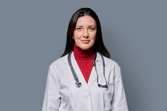 Portrait of serious female doctor in white lab coat with stethoscope on gray background