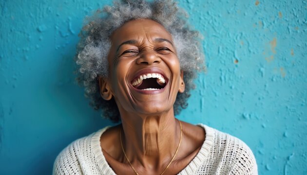 Joyful elderly african american woman with grey curly hair laughs heartily. Smiling senior person has eyes closed, head tilted back against bright blue wall backdrop. Genuine expression of happiness.