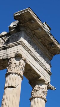 three weathered corinthian columns topped by ornately carved entablature floral reliefs contrasts sharply brilliant cloudless blue sky rome up close empire 