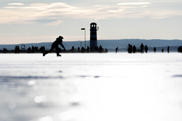 Eislaufen am zugefrorenen Neusiedler See in Podersdorf mit dem Leuchtturm im Hintergrund	