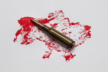 Fototapeta premium An outline of a map of Ukraine, painted in red paint, and a bullet on a white background, simulated blood