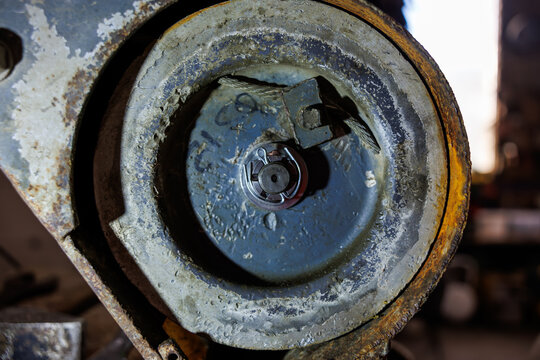 Close view of a worn pulley wheel shows castellated nut, cotter pin, and frayed steel cable at rim. Corroded paint and grime indicate long service in an industrial workshop.