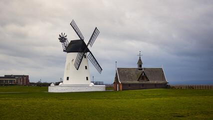 Lytham Windmill in Lancashire, United Kingdom, is in a landscape with atmospheric lighting and sky that illuminates the grassy surroundings. © alan1951