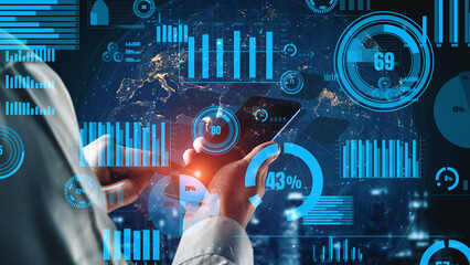 A businessman engages with a smartphone in a modern office, surrounded by digital graphs and charts that represent financial data and analytics in a futuristic setting. Xenic