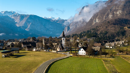 Winding Road to Stara Fuzina Village: Aerial View of Alpine Valley with Clouds on Mountains and Traditional Hayracks, Slovenia countryside