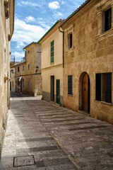 Sunlit narrow street with traditional stone houses in Alcudia old town Mallorca