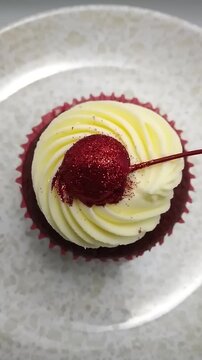 Top Down View of Red Velvet Cupcake topped with Cream Cheese Frosting and Glitter-dusted Cherry