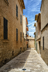 Sunlit narrow alley with traditional stone facades and shutters in Alcudia old town Mallorca