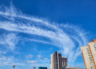 Above the city, in the beautiful blue sky, there are bizarre white streaks from a passing airplane.
