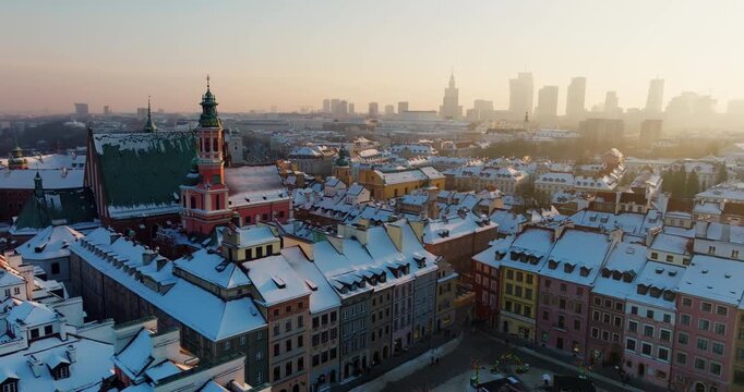 Cinematic drone view of Warsaw, Poland in winter. High angle establishing shot of snowy Old Town landmarks including Royal Castle and Cathedral with the modern downtown business skyline in sunny haze
