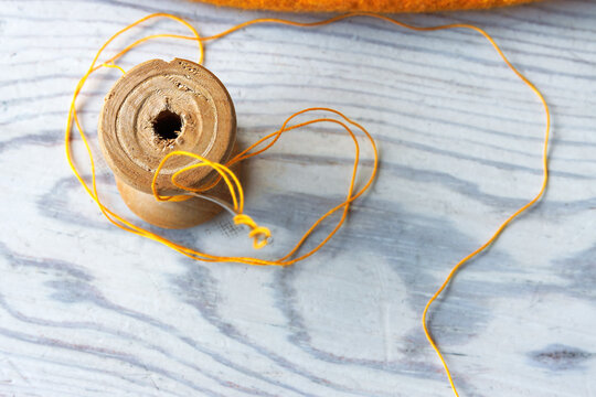 Top view of a yellow thread spool with loose thread on a light wooden tabletop with copy space
