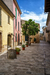 Historic stone well and traditional colorful houses in Sa Cisterna Alcudia old town