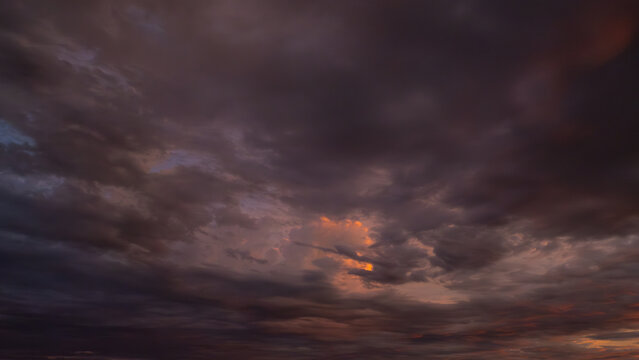 Breathtaking sunset featuring heavy, dark clouds illuminated by a fiery orange glow. A moody and dramatic sky filled with deep purple and warm golden textures