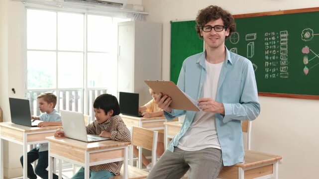 Caucasian teacher checking document and looking at camera at classroom. Diverse children sitting at learning about coding engineering prompt and generated AI. Cute student programing system. Pedagogy.