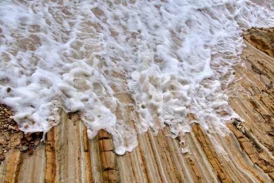 Natural background of layered sedimentary flysch rock and sea foam