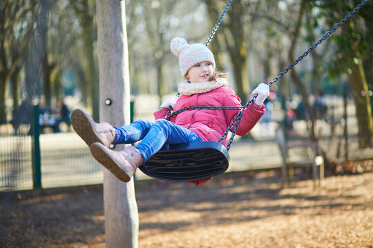 A young girl in a warm winter outfit having fun on a playground swing. Energetic outdoor childhood moment full of movement, joy, and active play.