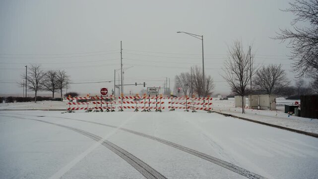 Wide view of intersection blocked by road closure barriers and warning signs during winter weather. traffic restrictions, public safety, caused by snow and road conditions.