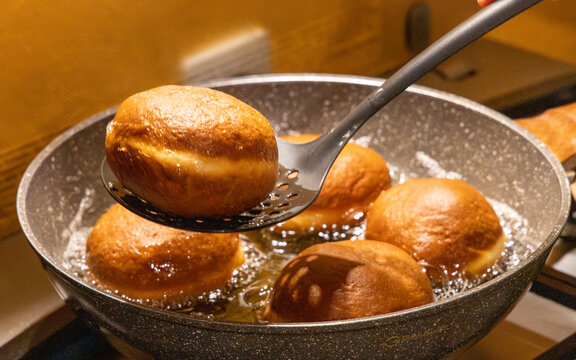 Taking out fresh golden doughnut from hot frying oil with skimmer spoon for traditional Fat Thursday dessert preparation and delicious homemade sweet pastry cooking.