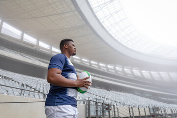 White and green rugby ball is resting against metal railing in modern covered stadium