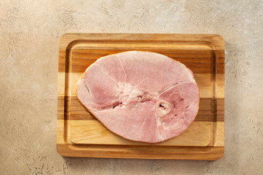 A top down view of a cooked bone in ham steak, on a wood board.