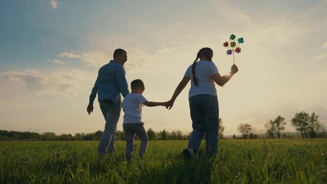 Family walking in field. Silhouette of family holding hands in a park. A dad and his children are walking toy. A field family strolling through a lifestyle.