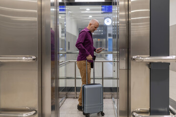 Businessman traveling with luggage checking phone in elevator © Jelena