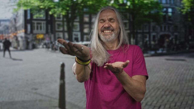 Man with long gray hair smiling and offering open palms toward camera on cobblestone street in city; warm welcome generosity joy.