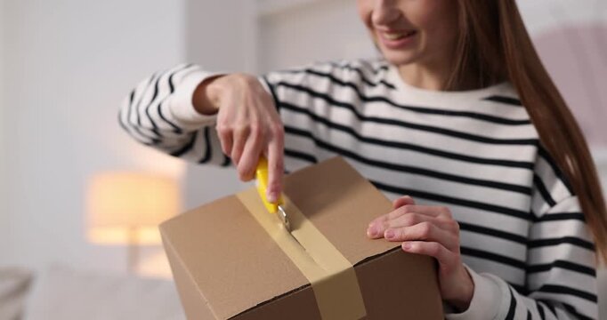 Woman opening parcel with knife at home, closeup