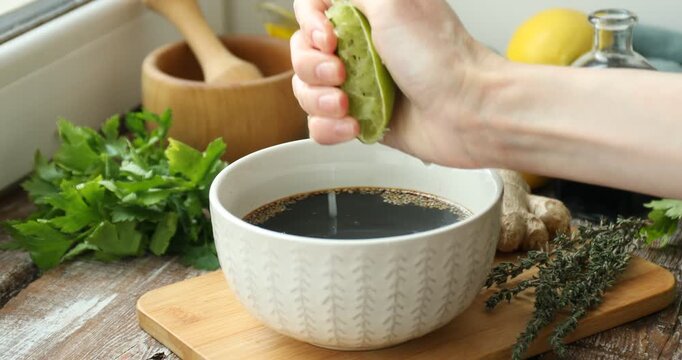 Woman squeezing lime juice into bowl with soy sauce marinade at wooden table, closeup