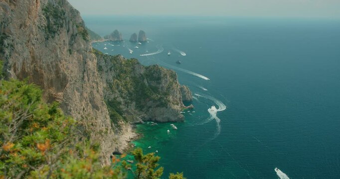 Boats moving along the blue sea near rocky cliffs and Faraglioni sea stacks in Capri Italy
