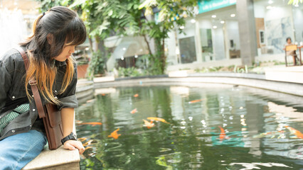 A young girl sitting beside a koi pond in a bright indoor environment.