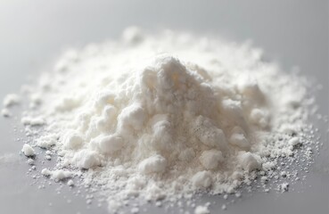 Heap of fine white powder, likely icing sugar, shown in close-up detail. The grainy texture forms small clumps against a neutral gray surface. This ingredient is perfect for baking.