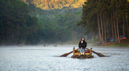 asian family by mother daughter tourist wearing black coat to cold and travel on bamboo rafting in lake with morning fog mist on water surface and camping tent at Pang Ung Reservoir in winter thailand