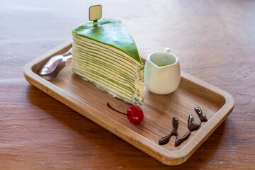 Matcha cake one piece with green tea soup in small cup and red cherry chocolate sauce with dual spoon in wood tray and brown wooden table with empty sign tag in cafe restaurant for sweet snack dessert