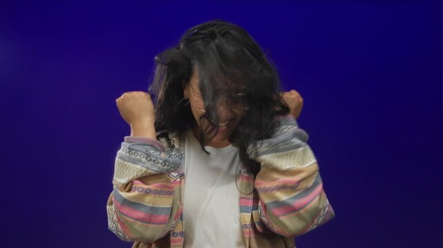 Woman pointing finger and smiling in a deep purple studio, wearing patterned jacket, round glasses and hoop earrings; joy celebration.