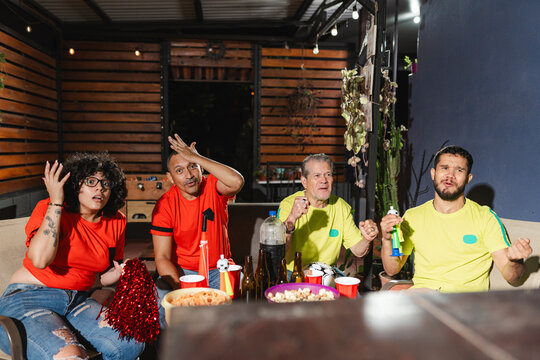 Horizontal shot of supporters in yellow jerseys cheering while rival fans in red jerseys argue and complain during a match