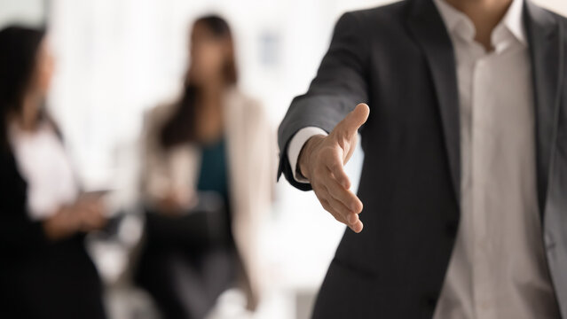 Close up confident businessman in formal suit extending his hand forward in welcoming handshake, gesture as beginning or finalizing successful business meeting or negotiation. Partnership, agreement