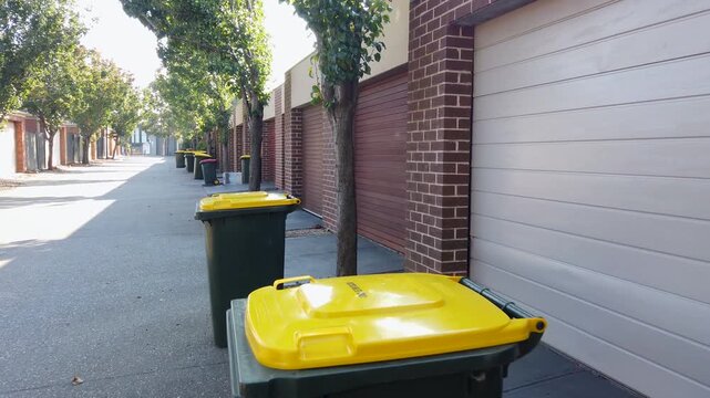 A row of residential garages along a suburban laneway, with wheelie bins lined up outside townhouses. Back-of-house street showing waste collection access, shared service lanes in Melbourne, Australia