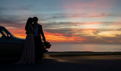 Generated AI: Eternal Romance at Dusk; Silhouetted Couple with Vintage Car and Flowers Against a Dramatic Coastal Sunset Backdrop.