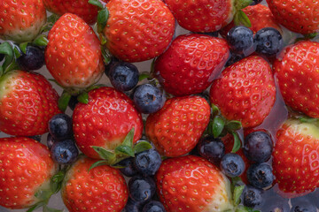 Obraz premium Fresh strawberries and blueberries soaking in water, vibrant red and deep blue colors, juicy texture, healthy summer fruit background.