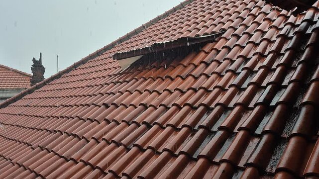 Leaking roof gutter during heavy rain, showing damaged drainage system, water flow on clay tiles, and home maintenance problem