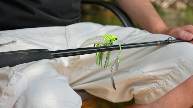 Man sitting with casting rod and attached perch spinner spoon blade with plastic paddle tail bait lure minnow to metal leader with braid for big bass or pike fishing. Sport fishing charter.