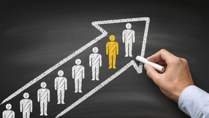A hand draws a chalk arrow with people icons on a blackboard, symbolizing leadership and success.