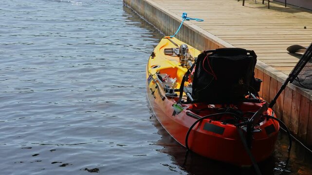 Fully rigger kayak watercraft mooring and tied to boat pier near cottage. Recreational watercraft, kayaking lake during tournament or fishing derby. Kayak water craft equipment for fishing activities.