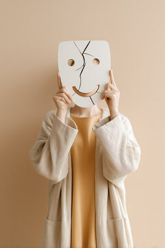 Surreal conceptual image of a person wearing a smiling mask holding a cracked mirror. Symbol of hypocrisy in warm muted tones, ideal for editorials, mental health topics, art projects and branding.